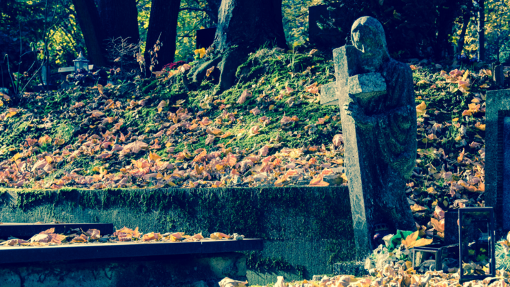 old stone statue of saint with cross in the cemetery