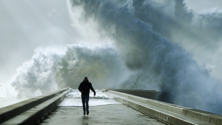 Lone man walking away from a huge series of waves in the background